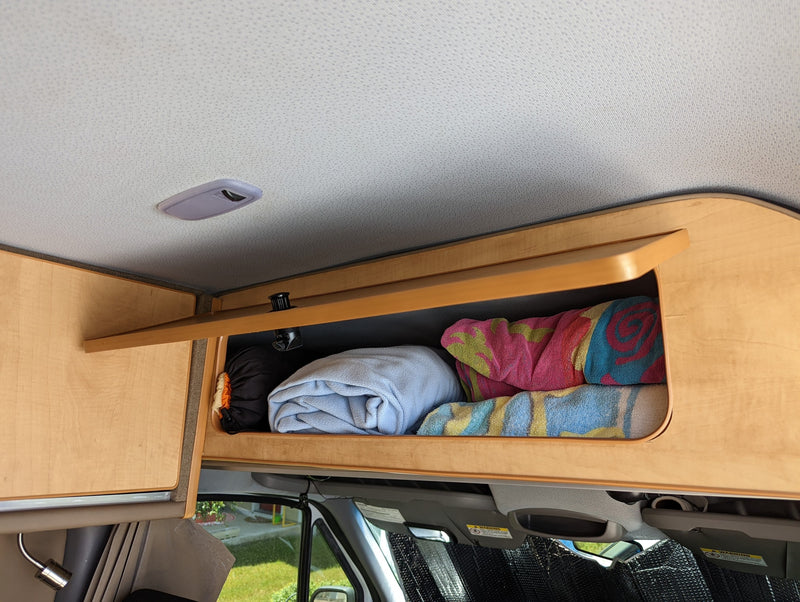 Inside an RV rental: an open wood overhead storage cabinet filled with folded blankets/towels. Practical interior for comfortable travel. — photo 17