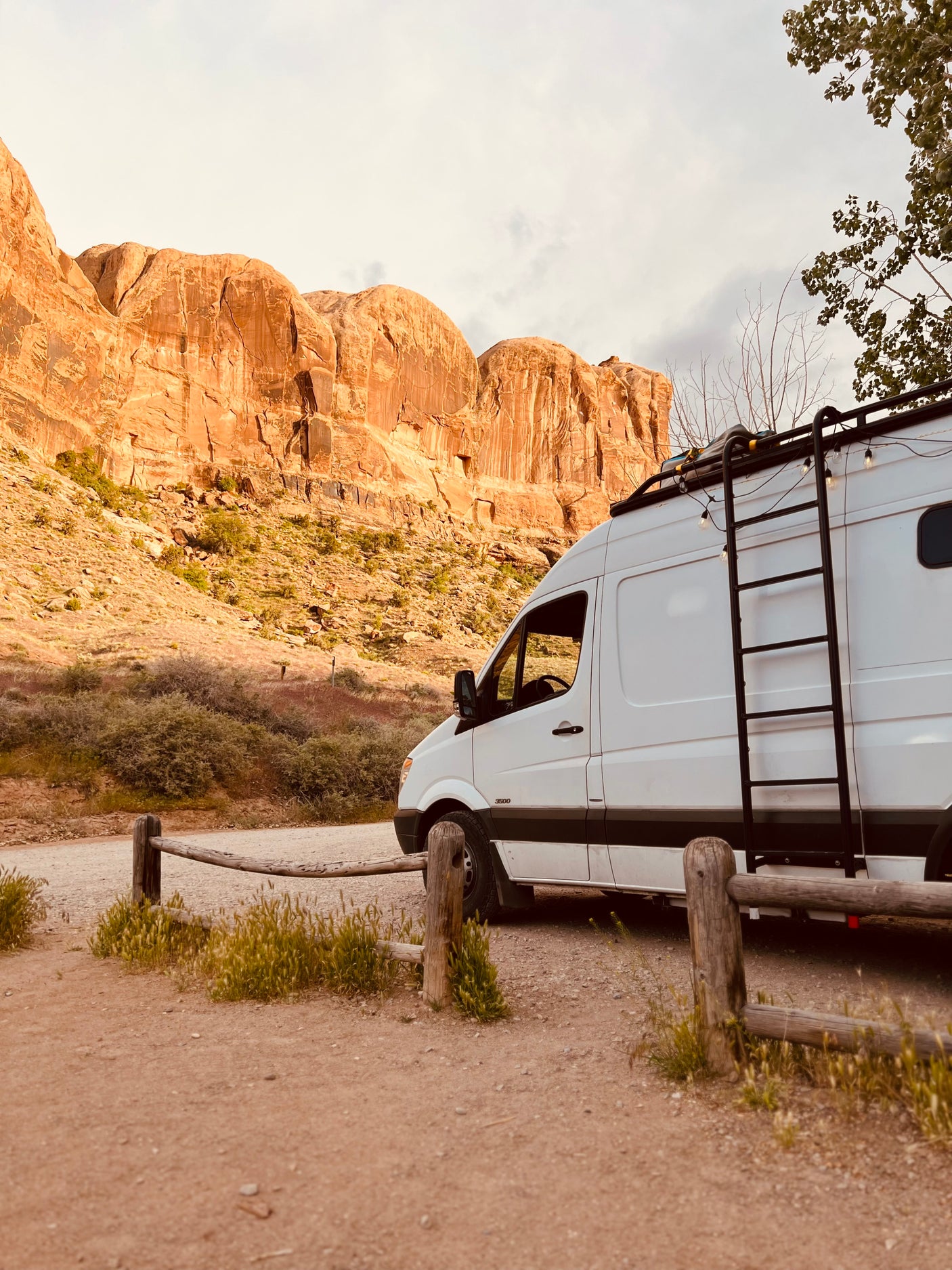 White camper van RV rental parked on a dirt road, facing towering desert rock formations.