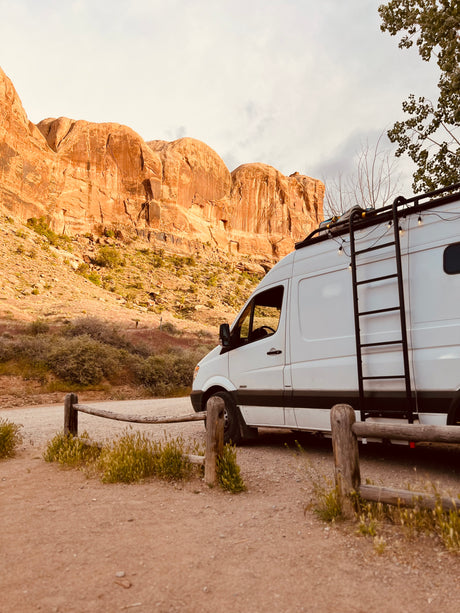 White camper van RV rental parked on a dirt road, facing towering desert rock formations.