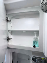 Inside an RV rental bathroom: a neat white cabinet with a blue soap bottle on a shelf. Shower head visible right.