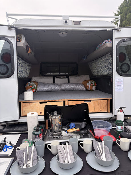 This rv rental offers a compact camper with an open rear, revealing a comfy sleeping area and a fully equipped outdoor kitchen.