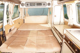 Cozy RV rental interior featuring a convertible bed, compact kitchenette, and windows revealing a scenic lake view.