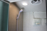 Compact RV rental shower interior: handheld shower head, ceiling light, ventilation fan, and wall-mounted mesh storage.