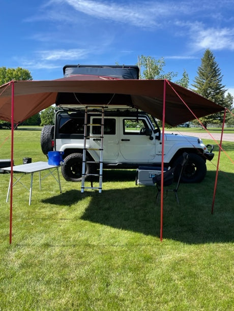 White Jeep SUV with extended awning & rooftop tent setup on grass, ready for outdoor RV rental adventures.