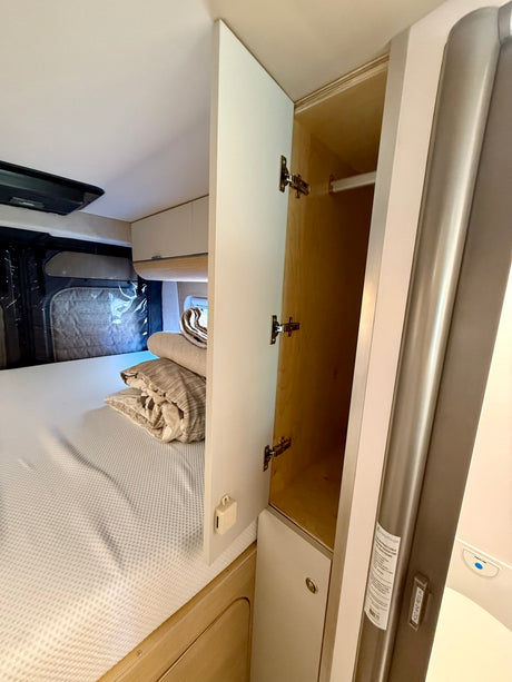 An RV rental interior view featuring a comfortable bed, open storage cabinet, and a space-saving retractable shower door.