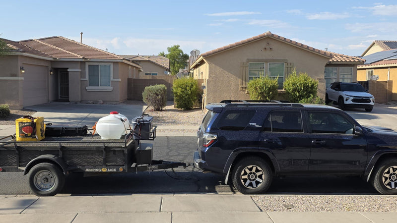 Dark blue SUV with utility trailer (water tank, gear) in a sunny neighborhood. No RV shown, but useful for rv rental trips. — photo 1