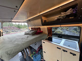 Cozy RV rental interior: comfy bed, compact kitchen, bike storage, and scenic nature views outside.
