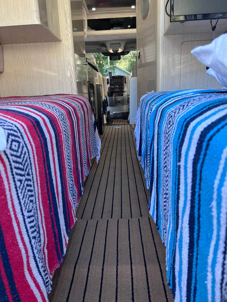 Cozy RV rental interior featuring two beds with patterned blankets & striped flooring, leading to the cockpit.
