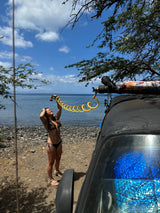 RV rental outdoor shower on a sunny beach. A woman in a bikini uses a yellow coiled hose by the sea.