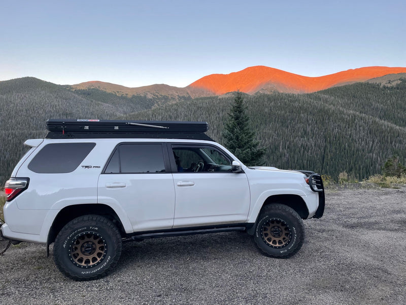 White Toyota 4Runner with a rooftop tent on a mountain road. Distant peaks glow orange at sunset. A great RV rental alternative for adventure. — photo 5