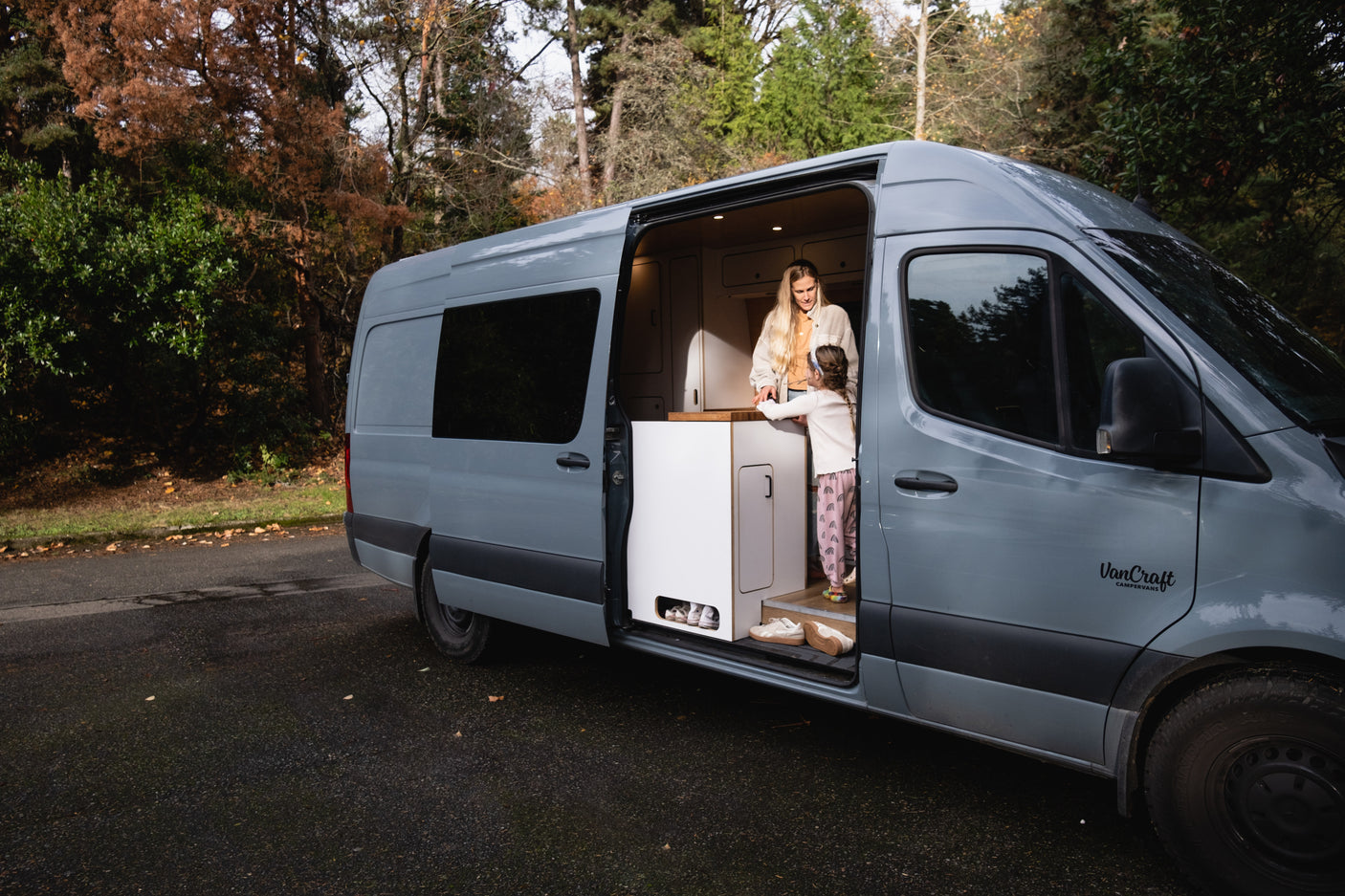 This RV rental shows a woman and child inside a grey camper van, enjoying its custom interior in a natural setting.