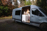 This RV rental shows a woman and child inside a grey camper van, enjoying its custom interior in a natural setting.