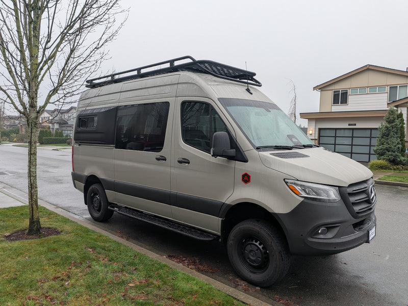 This custom light-colored Mercedes Sprinter camper van, likely an rv rental, is parked on a wet street on an overcast day. — photo 2