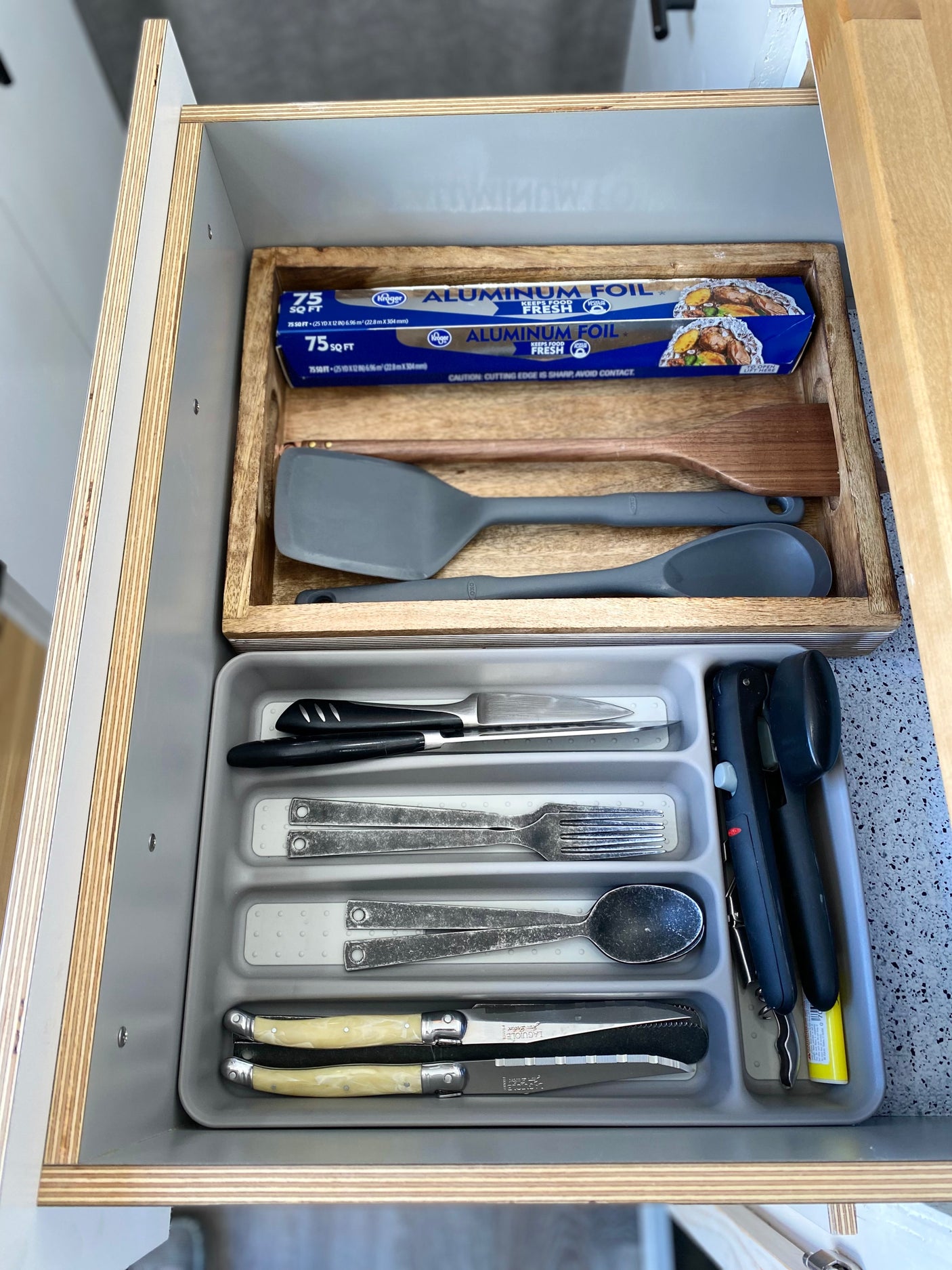 Organized kitchen drawer in an RV rental: cooking tools, cutlery, and aluminum foil, showcasing efficient compact living.