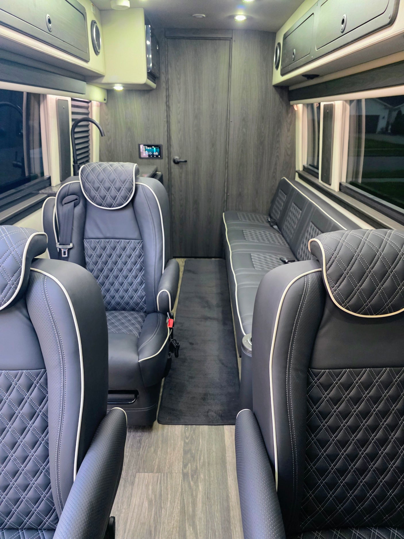 Spacious RV rental interior featuring luxury black leather captain's chairs, bench seating, and wood-look flooring.
