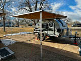 This RV rental teardrop trailer, with an extended awning, is parked at a snowy campsite under a blue sky, ready for adventure.