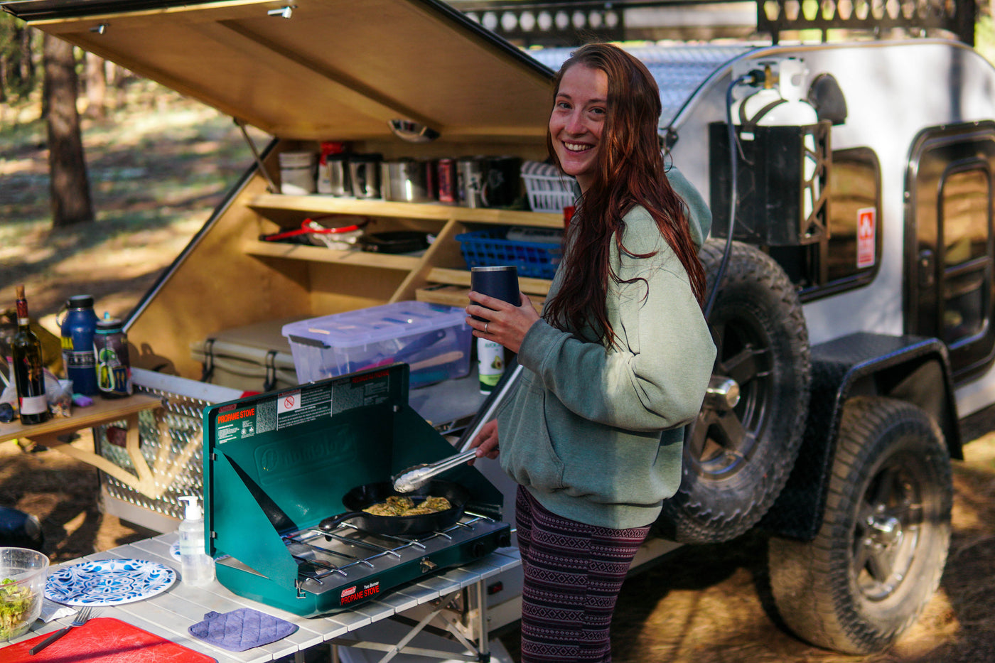 Happy woman cooks by her RV rental teardrop camper, enjoying the outdoor kitchen setup. — photo 17