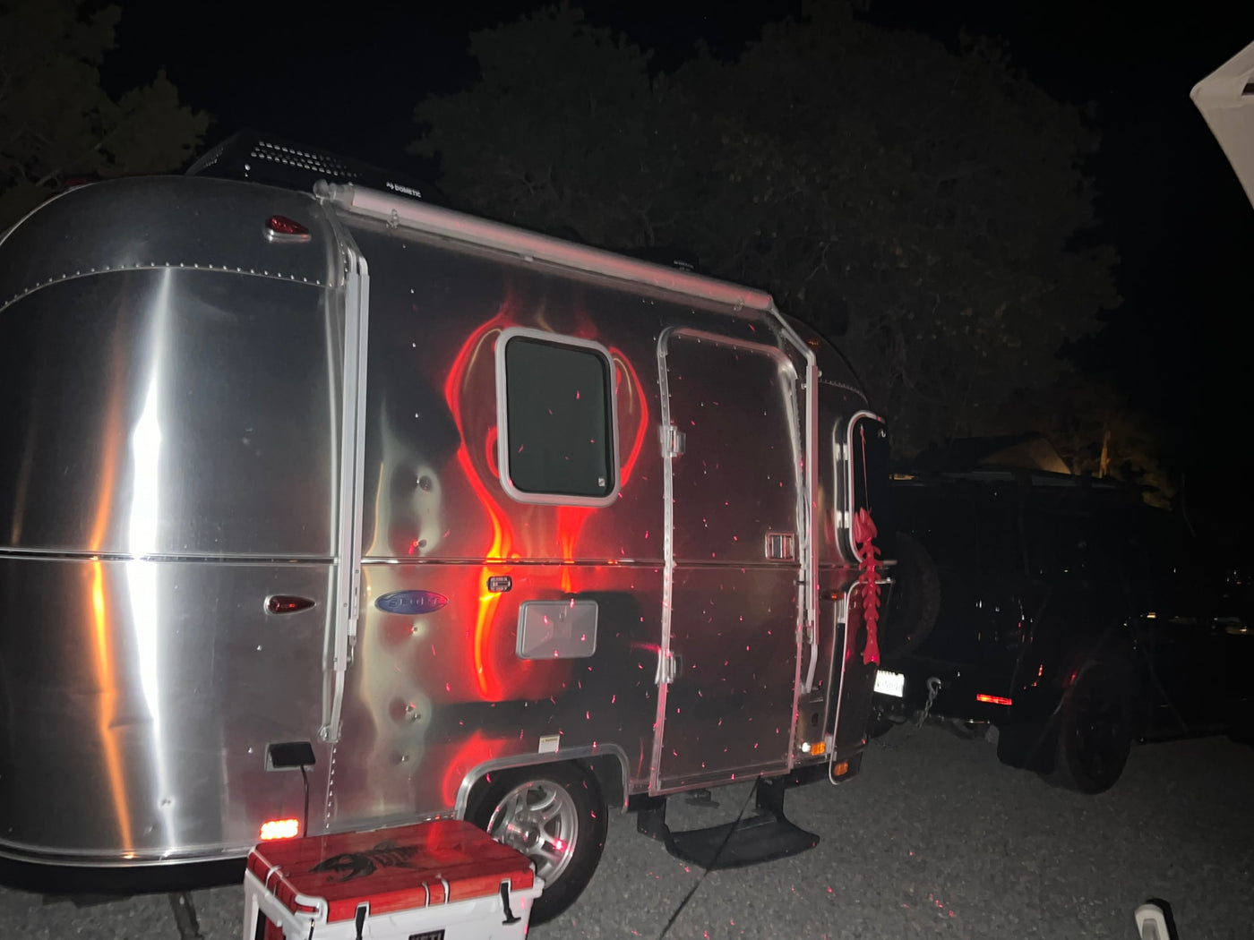 Night view of a shiny Airstream RV rental, covered in red laser light patterns, parked next to a cooler for camping. — photo 8