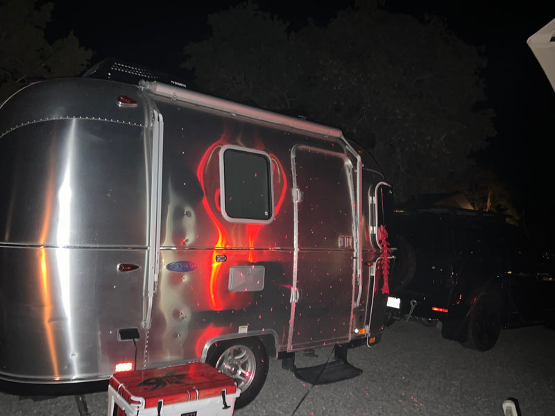 Night view of a shiny Airstream RV rental, covered in red laser light patterns, parked next to a cooler for camping. — photo 8