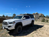 A white Toyota Tacoma truck with an overland camper setup, parked in a sunny, rocky landscape. Perfect for your next RV rental adventure.