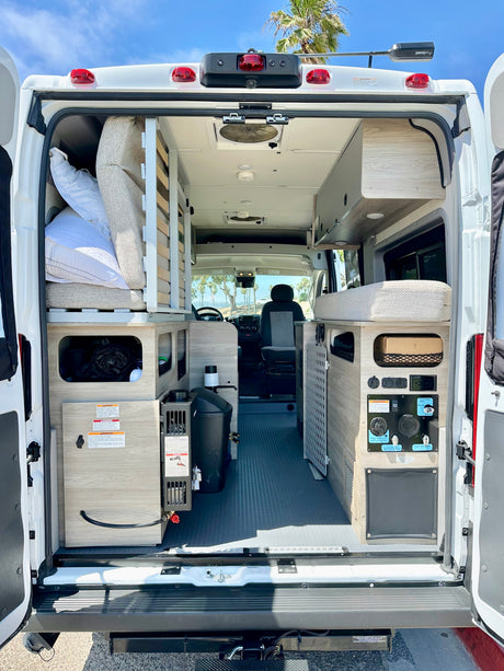 View from the rear of an **rv rental** camper van, showcasing custom interior layout with beds, storage, and water system.