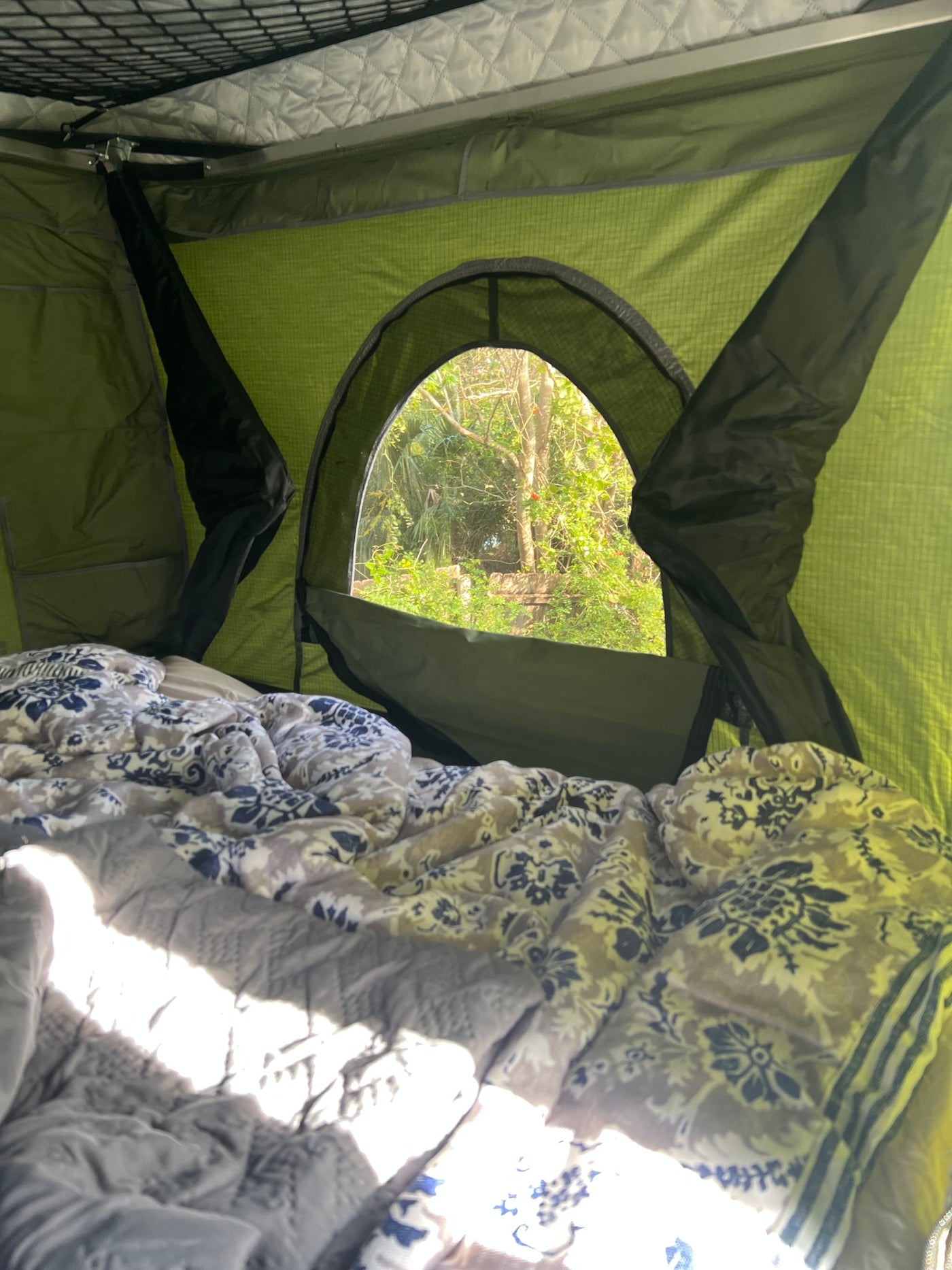 Inside a comfortable RV rental, patterned bedding under sunlight, with an arched window view of lush nature. — photo 18