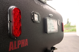 Rear of an Alpha **rv rental**: red tail light, Nilight LED, and license plate area on textured black finish for rugged outdoor trips.