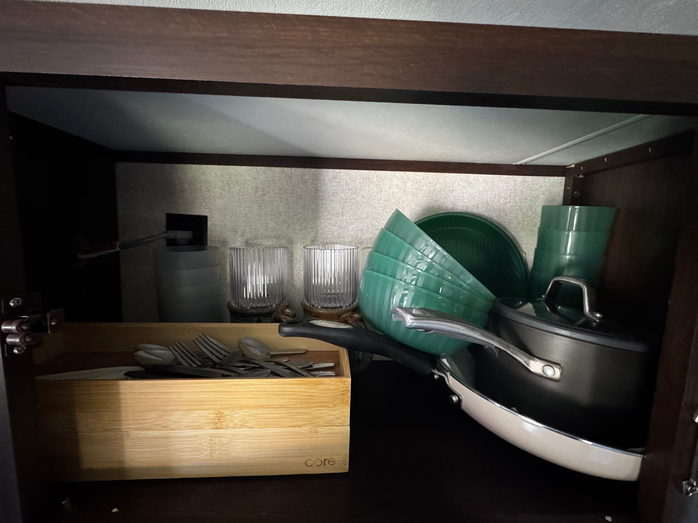 Compact kitchen storage in an RV rental: green dishes, pots, and utensils in a wooden organizer.