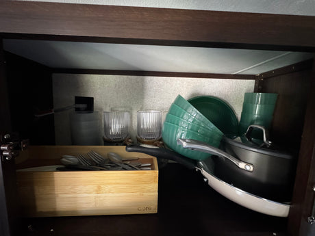 Compact kitchen storage in an RV rental: green dishes, pots, and utensils in a wooden organizer.