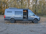 Rugged gray Mercedes Sprinter camper van, ideal for RV rental adventures. Parked on a leaf-strewn path with open door.