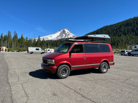 Red camper van with rooftop tent in a scenic mountain lot, perfect for your next RV rental trip.