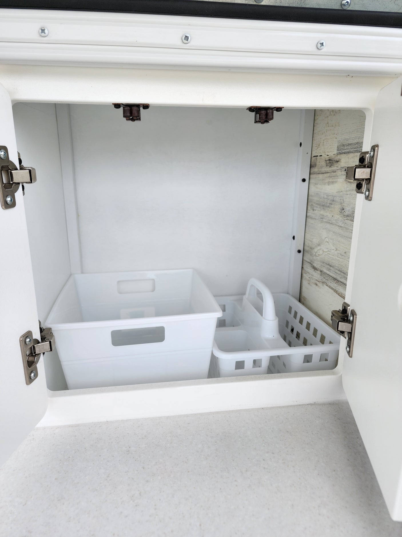 Inside an RV rental: A clean, open white cabinet revealing two plastic organizers on a speckled counter.