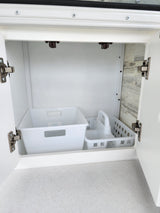 Inside an RV rental: A clean, open white cabinet revealing two plastic organizers on a speckled counter.