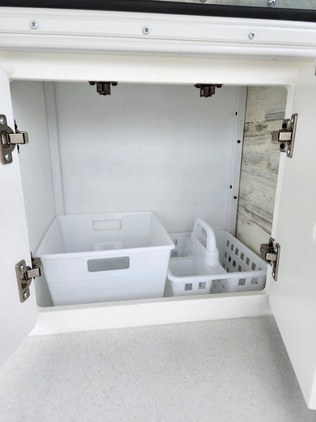 Inside an RV rental: A clean, open white cabinet revealing two plastic organizers on a speckled counter.