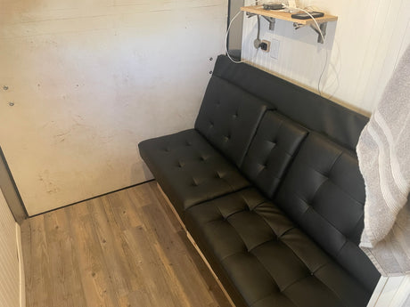 Cozy RV rental interior featuring a black futon, charging shelf, and wood-look flooring.