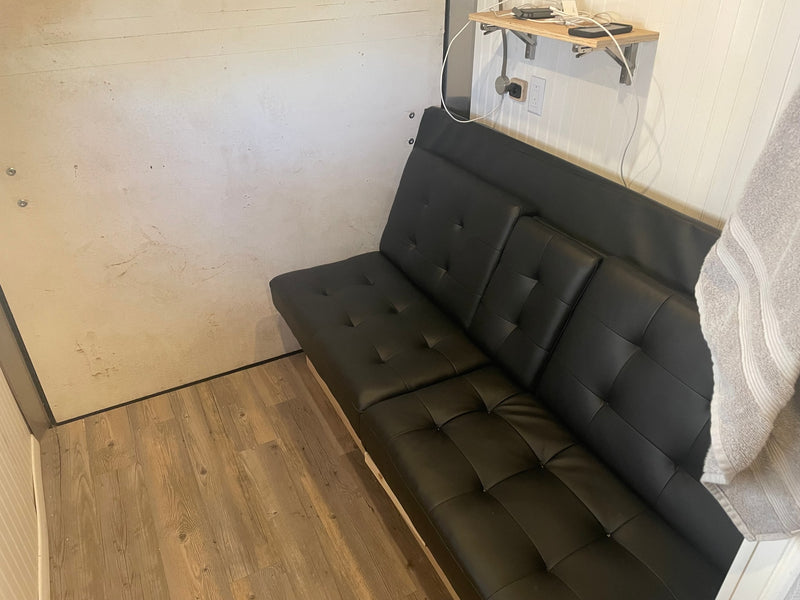 Cozy RV rental interior featuring a black futon, charging shelf, and wood-look flooring. — photo 2