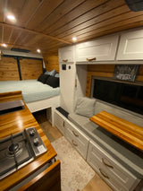 Inside a stylish RV rental: wood-paneled walls, a cozy bed, compact kitchen, and versatile seating.