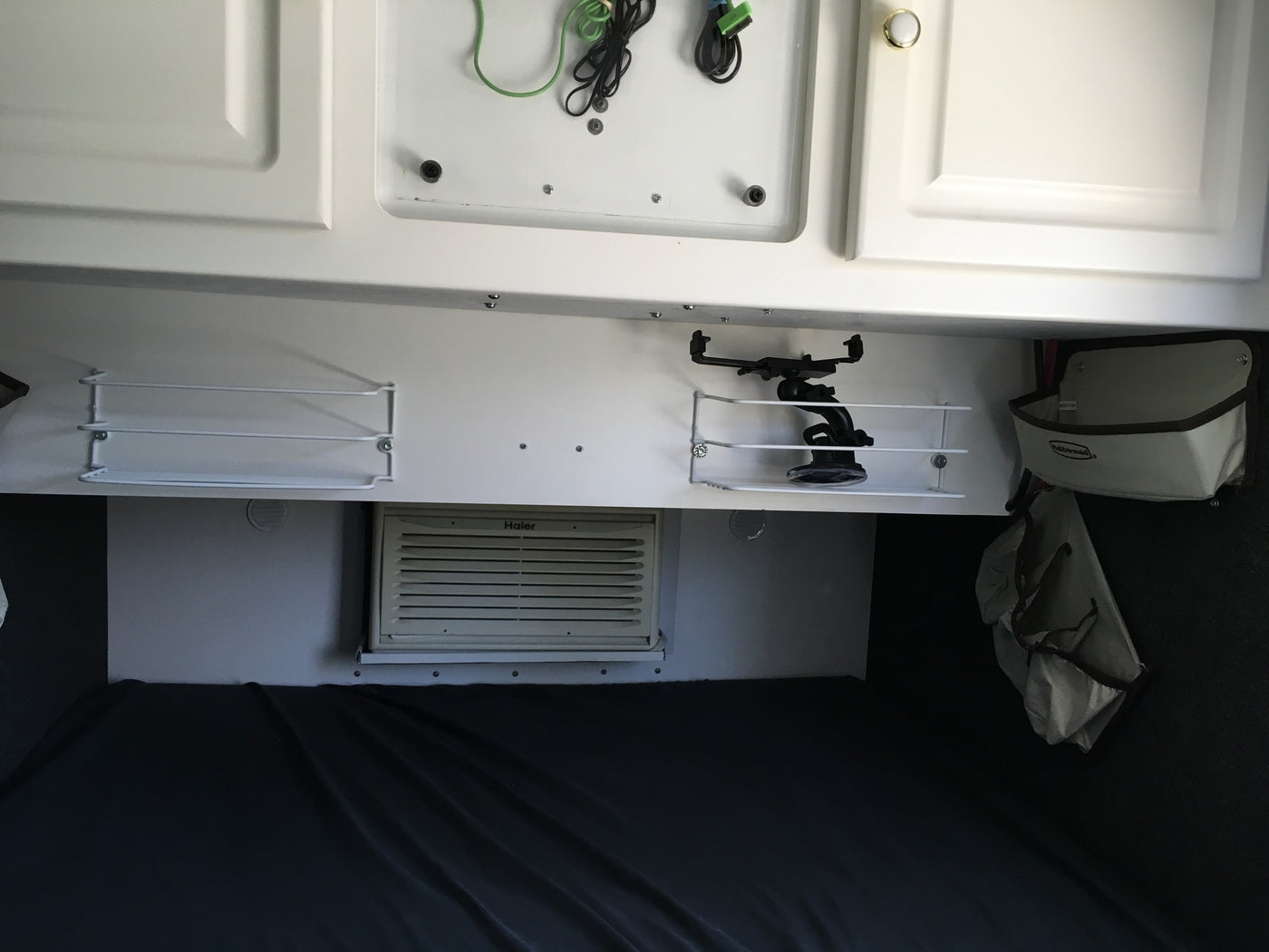 RV rental interior: white overhead cabinets, mounted shelves, a Haier AC unit, and a cozy bed area for travelers. — photo 10