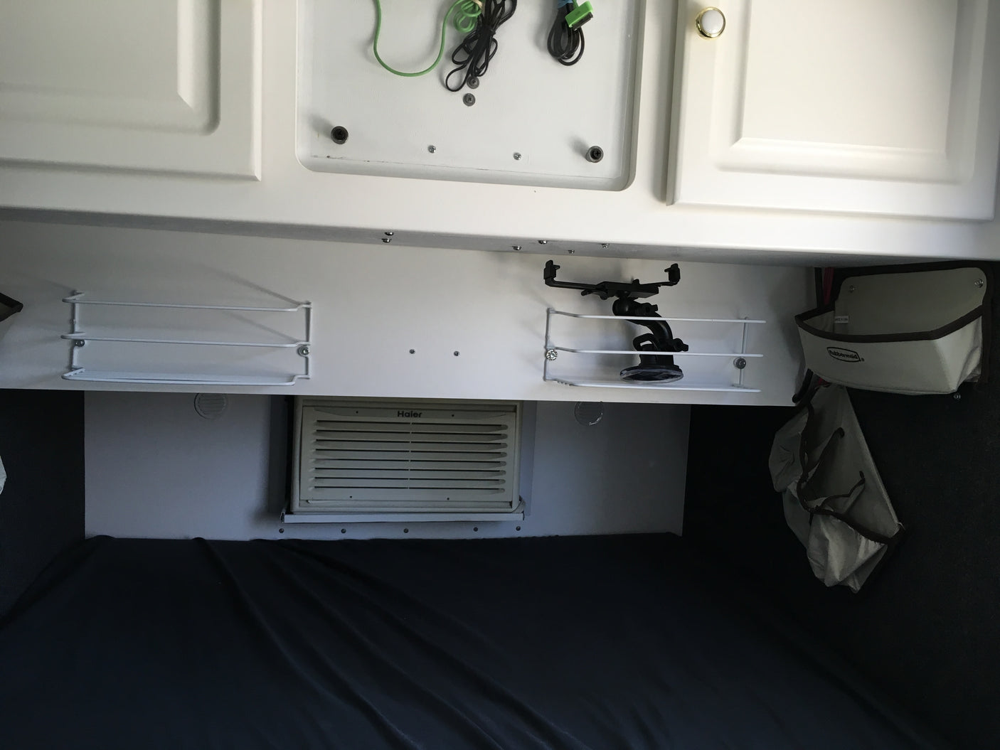 RV rental interior: white overhead cabinets, mounted shelves, a Haier AC unit, and a cozy bed area for travelers.