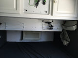 RV rental interior: white overhead cabinets, mounted shelves, a Haier AC unit, and a cozy bed area for travelers.
