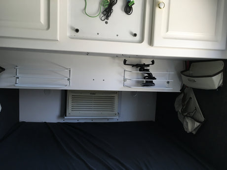RV rental interior: white overhead cabinets, mounted shelves, a Haier AC unit, and a cozy bed area for travelers.