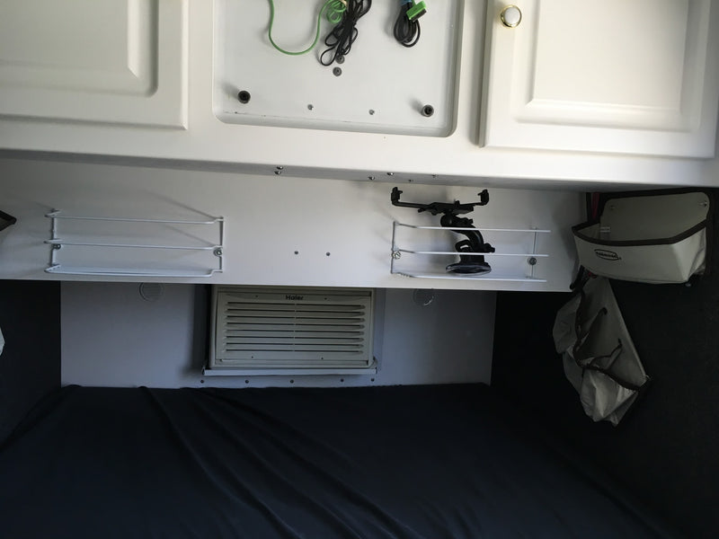 RV rental interior: white overhead cabinets, mounted shelves, a Haier AC unit, and a cozy bed area for travelers. — photo 10