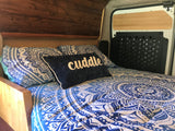 Cozy RV rental bed with blue mandala bedding and "cuddle" pillow. Features warm wooden interior and details.