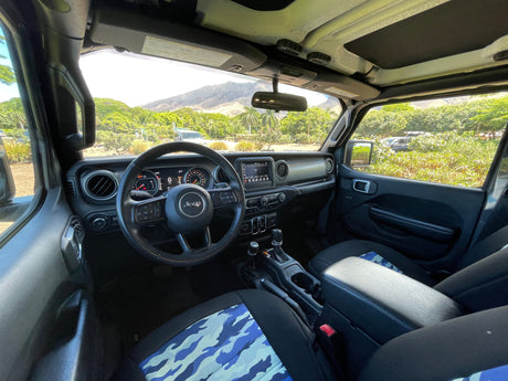 Jeep Wrangler interior with blue camo seats, perfect for an RV rental adventure. Scenic mountains and lush greenery visible outside.