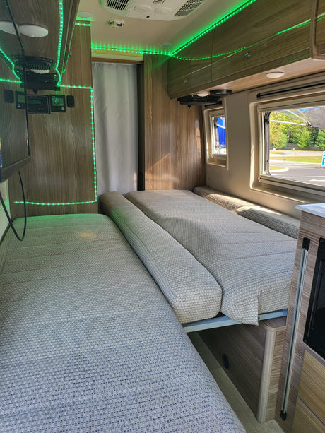 Interior of an **RV rental** featuring two long padded beds/benches, accented by bright green LED strip lights and wood panels.