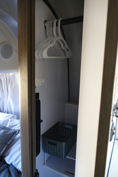 RV rental closet: White hangers, an LED light, and a dark basket on a shelf provide compact storage. Bedding visible left.