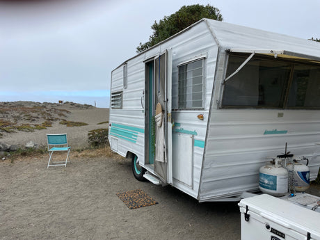 This vintage Land Commander RV rental offers a serene beachside escape, parked on sandy terrain under a cloudy sky.