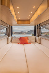 Relax in this modern RV rental bed with stunning lake and mountain views. Features light cushions and overhead lighting.