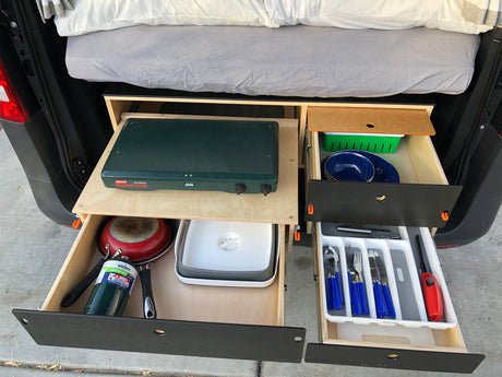RV rental's pull-out kitchen: Coleman stove, pan, plates, and blue utensils in organized drawers.