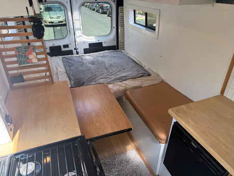 Inside an RV rental: a compact living space featuring a bed, kitchenette, and bench seating, ready for adventure.